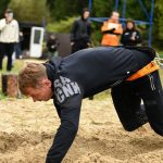 Man demonstrating strength as he crawls in a sand obstacle course with a body harness outdoors.